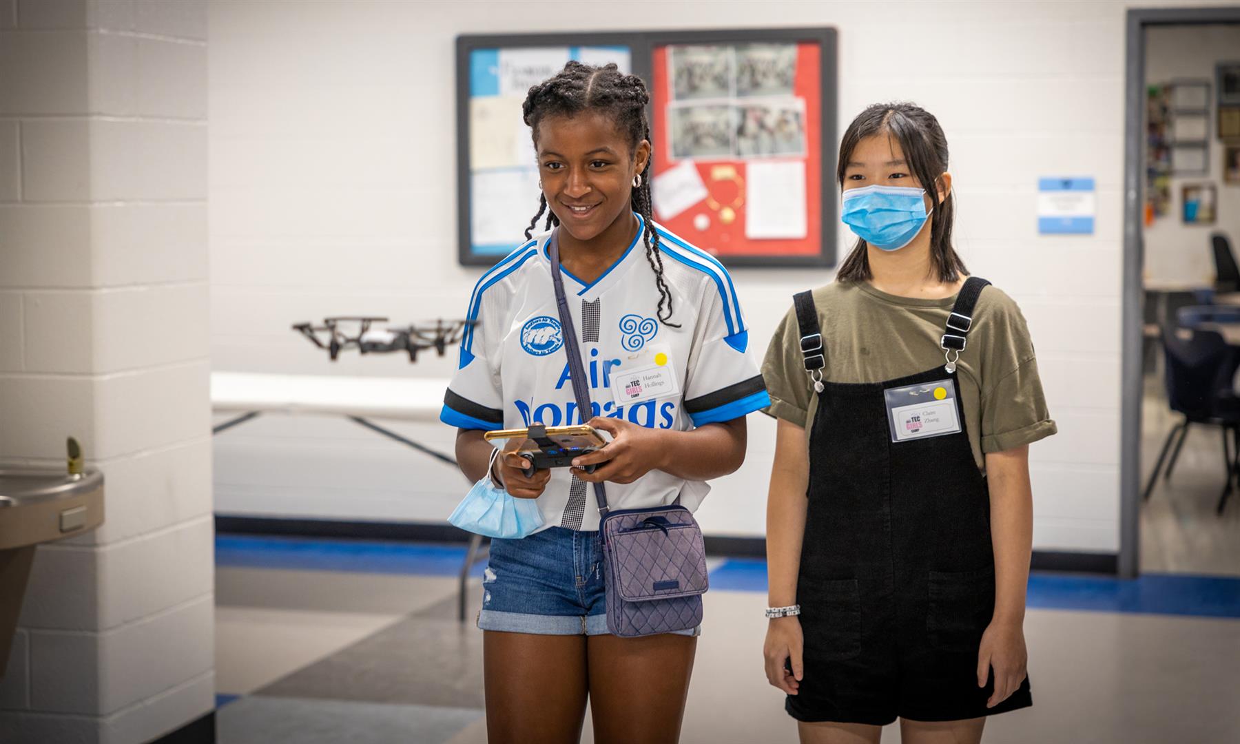 Two girls fly a drone in a hallway